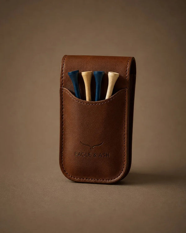A brown leather golf club headcover pouch by Eagle & Ash, holding four golf clubs with blue and beige shafts, set against a solid brown background.