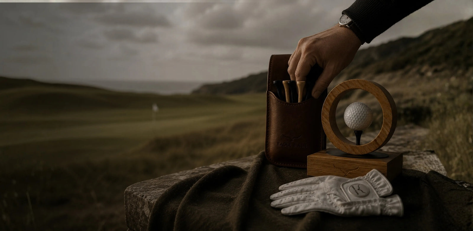 Golf accessories including a club, ball, and glove on a bag with a golf course in the background